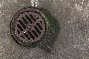Close-up photo of a rusty drain grate with moss, offering a textured urban look.